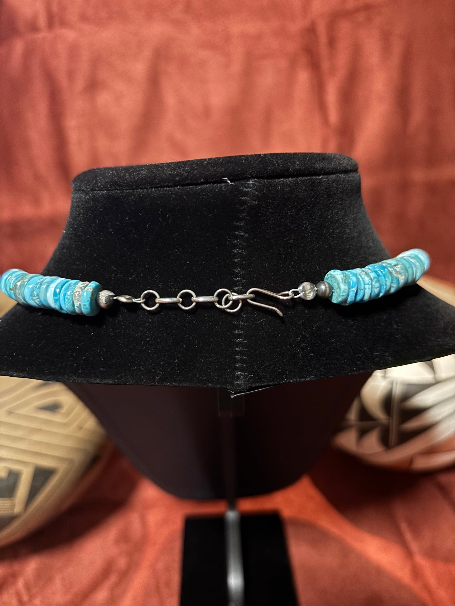Turquoise beaded necklace on a black mannequin head with a rustic background
