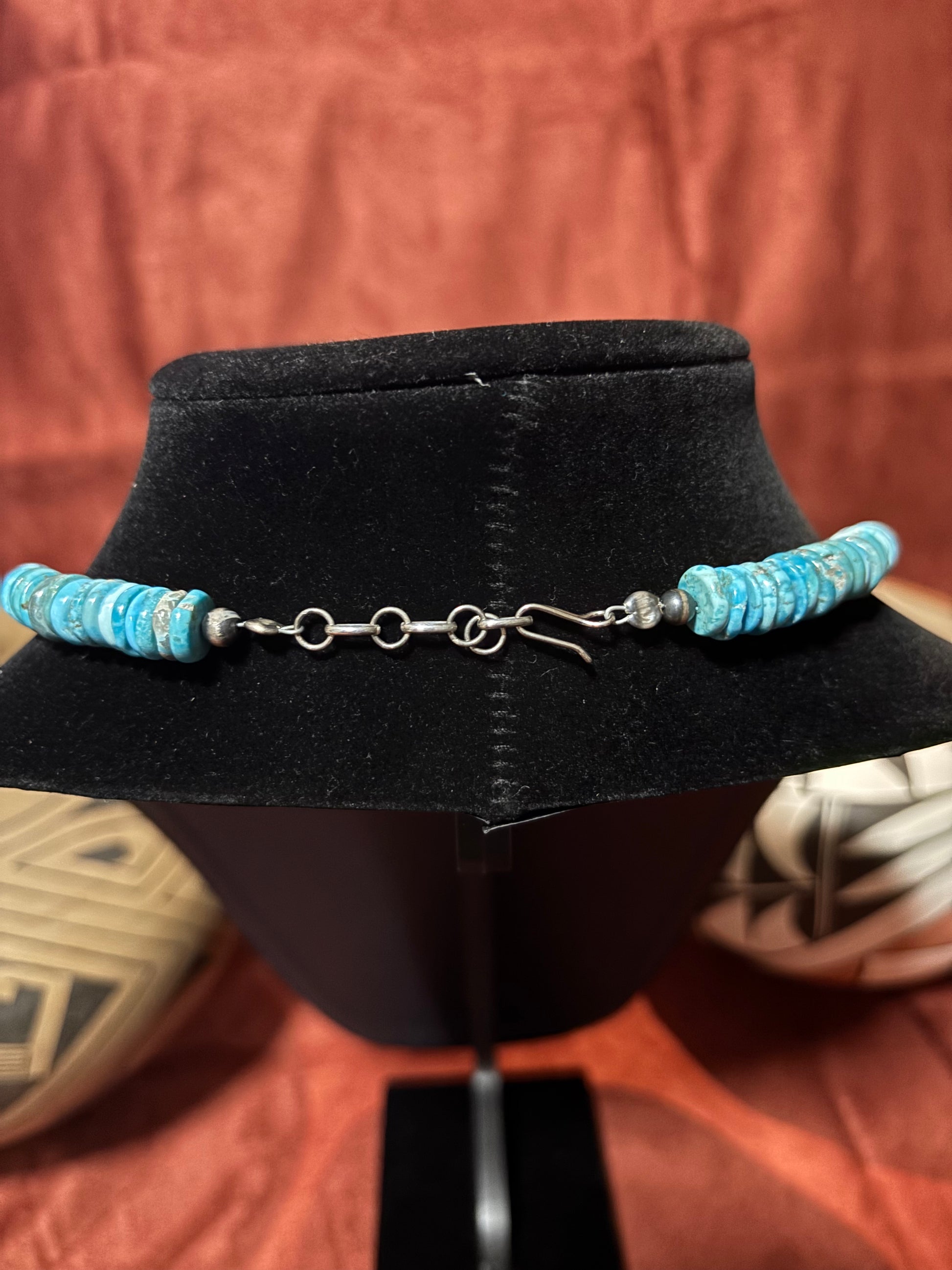 Turquoise beaded necklace on a black mannequin head with a rustic background